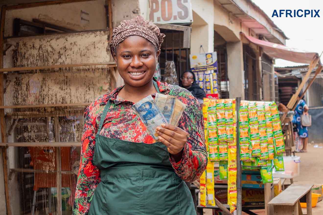 Joyful African Woman Holding Naira Front of Her Shop